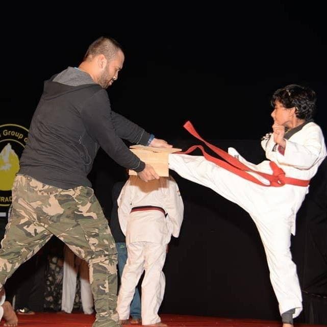 A young black-belt student executing a high side kick, breaking a board on stage.